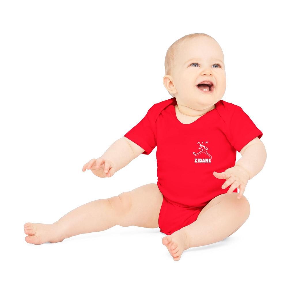 Body bébé rouge à manches courtes porté par un bébé assis, petit motif AIR ZIDANE côté cœur.